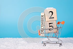 Sales presents on Christmas day concept. Close up photo of toy miniature small shopping cart full of wooden calendar cubes wheels