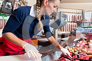 Sales woman in butcher shop putting different kinds of meat in display