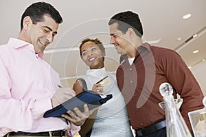 Salesman Calculating Bill While Couple Holding Credit Card In Store