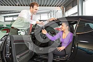 Salesman in car dealership sells automobile to customer