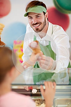 Salesman in confectionery provides ice cream to girl