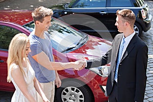 Salesman and couple shaking hands by car