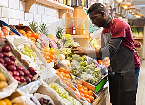 Salesman filling counter with vegetables and fruits