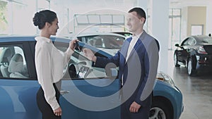 The salesman gives a car keys to happy businesswoman in the car dealership