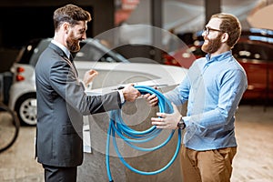 Salesman giving cable for electric car charging to a client