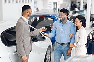 Salesman Giving Car Key To Buyers For Test-Drive In Dealership