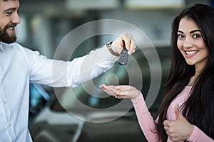 Salesman handing car keys to smiling woman in showroom