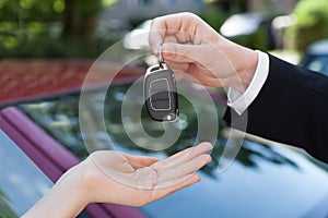 Salesman handing key to woman by new car