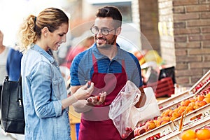 Salesman helping customer to choose some types of fruits in health grocery shop.