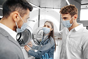 Salesman in hypermarket wearing medical mask demonstrates his clients a new washing machine