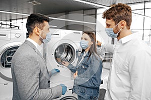 Salesman in hypermarket wearing medical mask demonstrates his clients a new washing machine