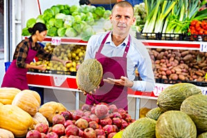 Salesman offering ripe melon in fruit and vegetable store