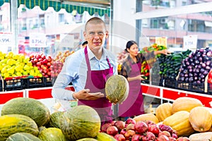 Salesman offering ripe melon in fruit and vegetable store