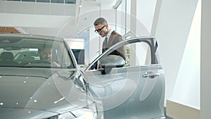 Salesman opening car door for buyer selling new automobile in dealership