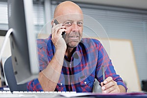 salesman sat at computer desk talking on smartphone