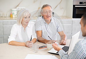 Salesman seller shows on laptop details of purchase to elderly couple.