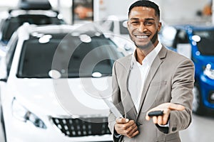 Salesman Selling Car Offering Key To Camera In Dealership Showroom