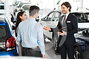 Salesman Selling Car To Customers In Dealership Showroom