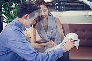 Salesman showing a contract detail to happy young attractive Asian millennials girl after her bought a new car at car dealershi