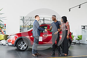 Salesman showing new car to african couple in showroom