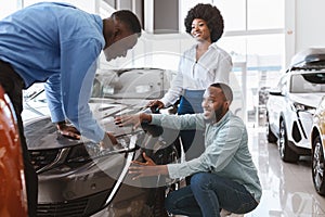 Salesman talking to young black couple, showing them new luxury car at auto dealership