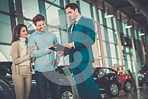 Salesman talking to a young couple at the dealership showroom.