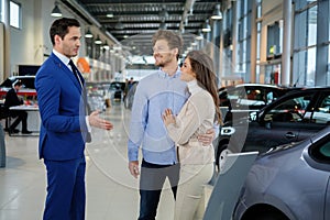 Salesman talking to a young couple at the dealership showroom.