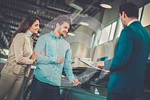 Salesman talking to a young couple at the dealership showroom.