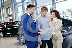 Salesman talking to a young couple at the dealership showroom.