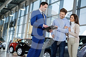 Salesman talking to a young couple at the dealership showroom.