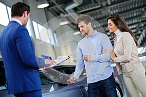 Salesman talking to a young couple at the dealership showroom.