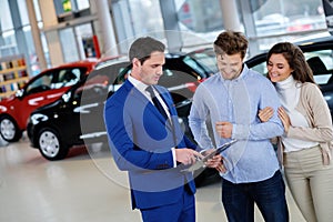 Salesman talking to a young couple at the dealership showroom.