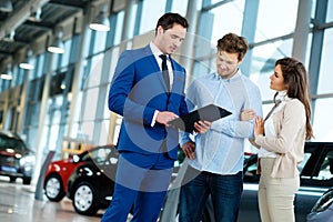 Salesman talking to a young couple at the dealership showroom