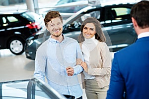 Salesman talking to a young couple at the dealership showroom