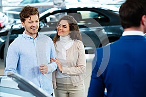 Salesman talking to a young couple at the dealership showroom