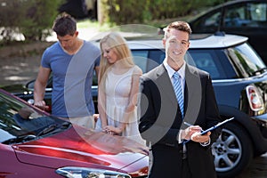 Salesman writing on clipboard with couple looking at car