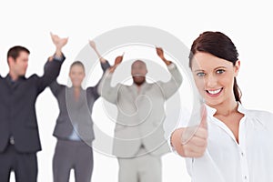 Saleswoman with cheering colleagues giving thumb up