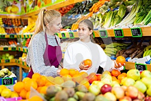 Saleswoman helping teenage girl to choose oranges in supermarket