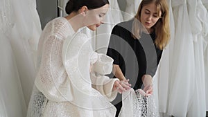 A saleswoman helps a young woman choose a wonderful wedding dress.