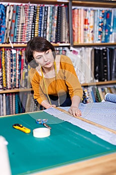 Saleswoman measuring and cutting off piece of cloth