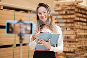 Saleswoman recording promo video about wood and products at storehouse