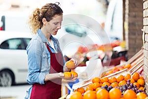 Saleswoman selecting fresh fruit and preparing for working day in health grocery shop.