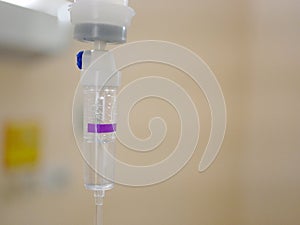 Saline drop in a drip chamber being infused with a patient room defocus background