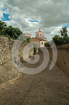 sAlley in a cloudy day with stone walls going towards the Santa Maria la Mayor Church and steeple at Trujillo