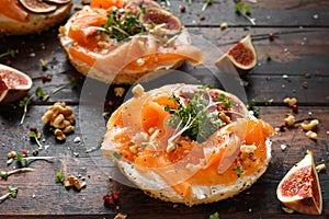 Salmon Bagel Sandwich with figs, cress salad, walnuts, cream cheese and grain on rustic wooden background. healthy