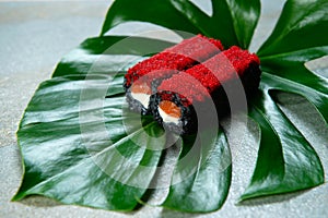 Salmon Black rice sushi roll with cattle fish inks on tropical leaf. Roll with cream cheese and red flying fish roe Tobiko