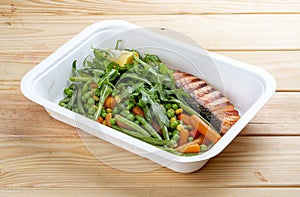 Salmon with blanched vegetables. Healthy diet. Takeaway food. On a wooden background