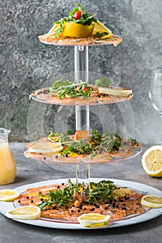 Salmon carpaccio with lemon and rocket on a cake stand, italian starter, antipasti
