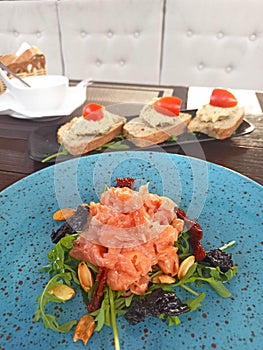 Salmon carpaccio on a turquoise plate and three slices of foie gras with cherry tomatos