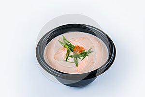 Salmon cream soup with salmon fillet pieces, red caviar served in plastic delivery bowl isolated on gray background